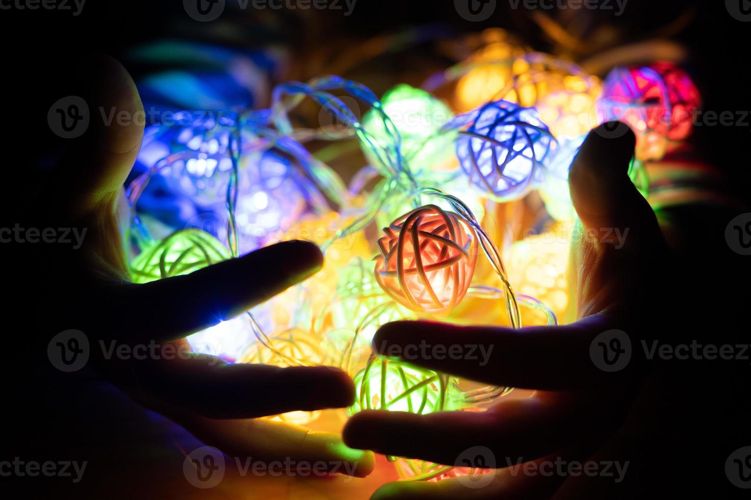 niño sosteniendo una guirnalda en las manos, brillando con coloridas luces multicolores en la noche foto