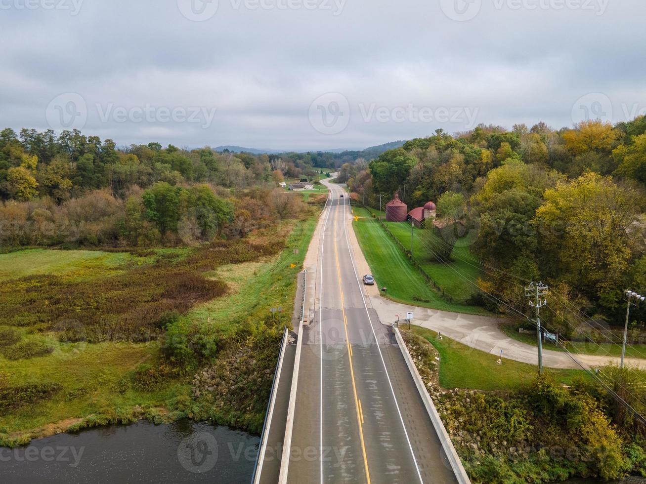 bridge over the river with rural road in autumn with green grass and tress shadows from mountains serve road entering highway photo