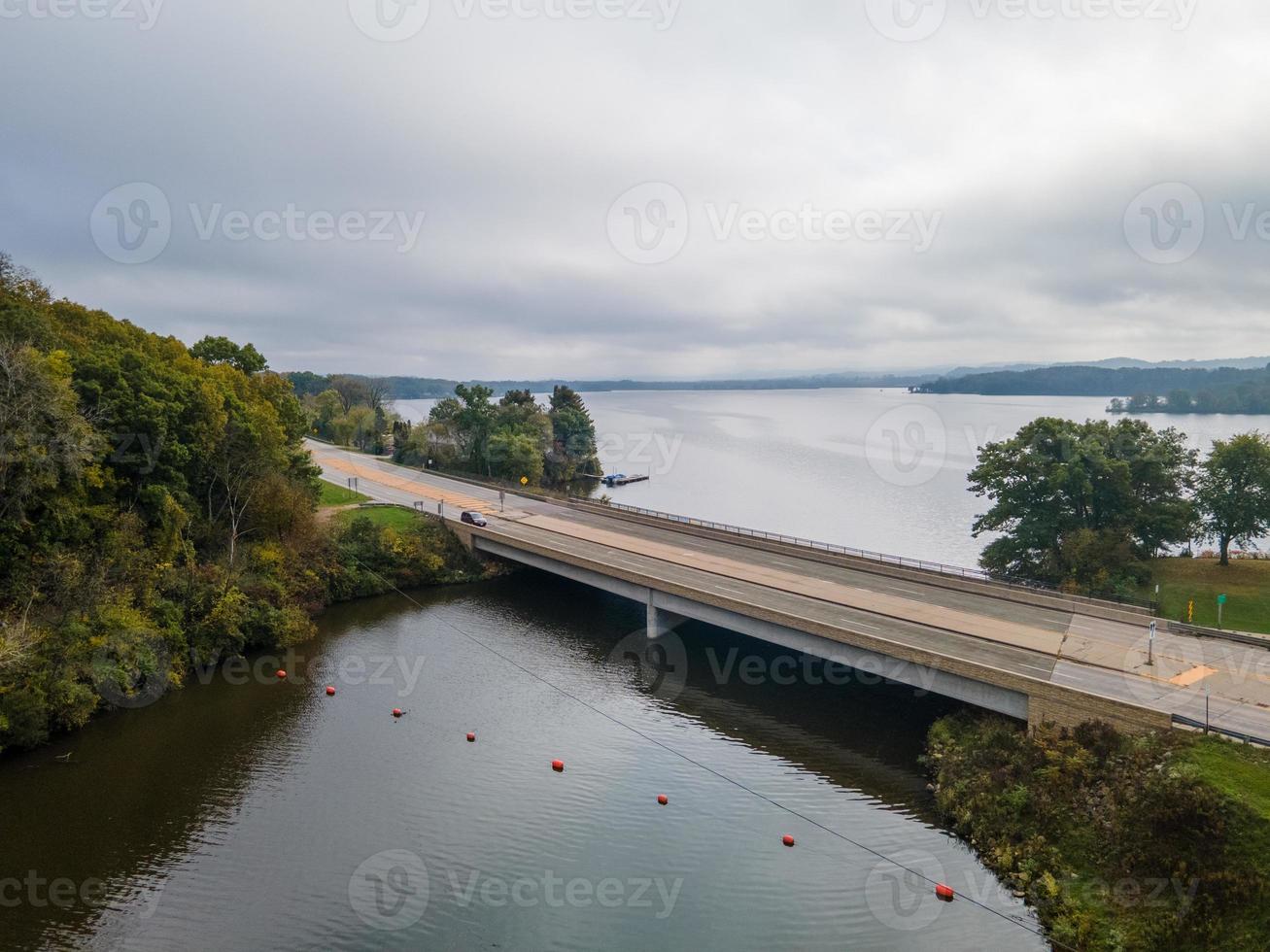 Puente rural sobre la entrada al hermoso lago en el medio oeste a principios de otoño línea de boyas que marcan la zona segura de árboles cambiando de color foto