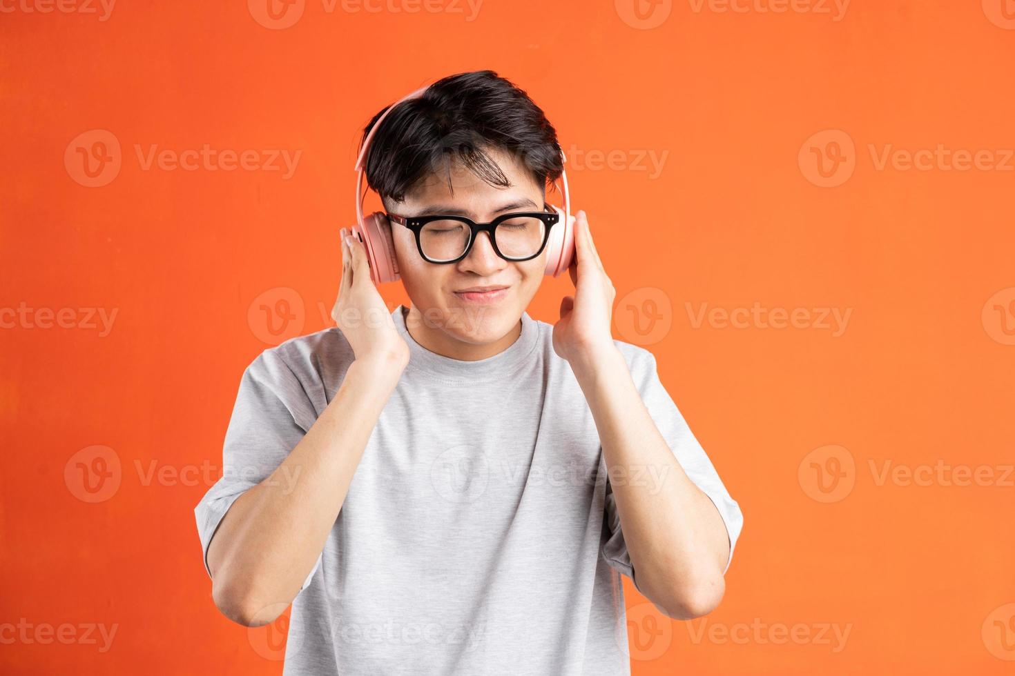 Retrato de joven asiático escuchando música con auriculares, aislado sobre fondo naranja foto