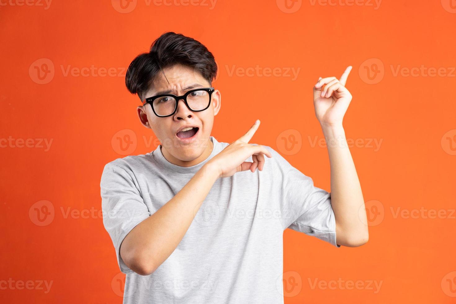 Portrait of young asian man pointing and confusing expression, isolated on orange background photo