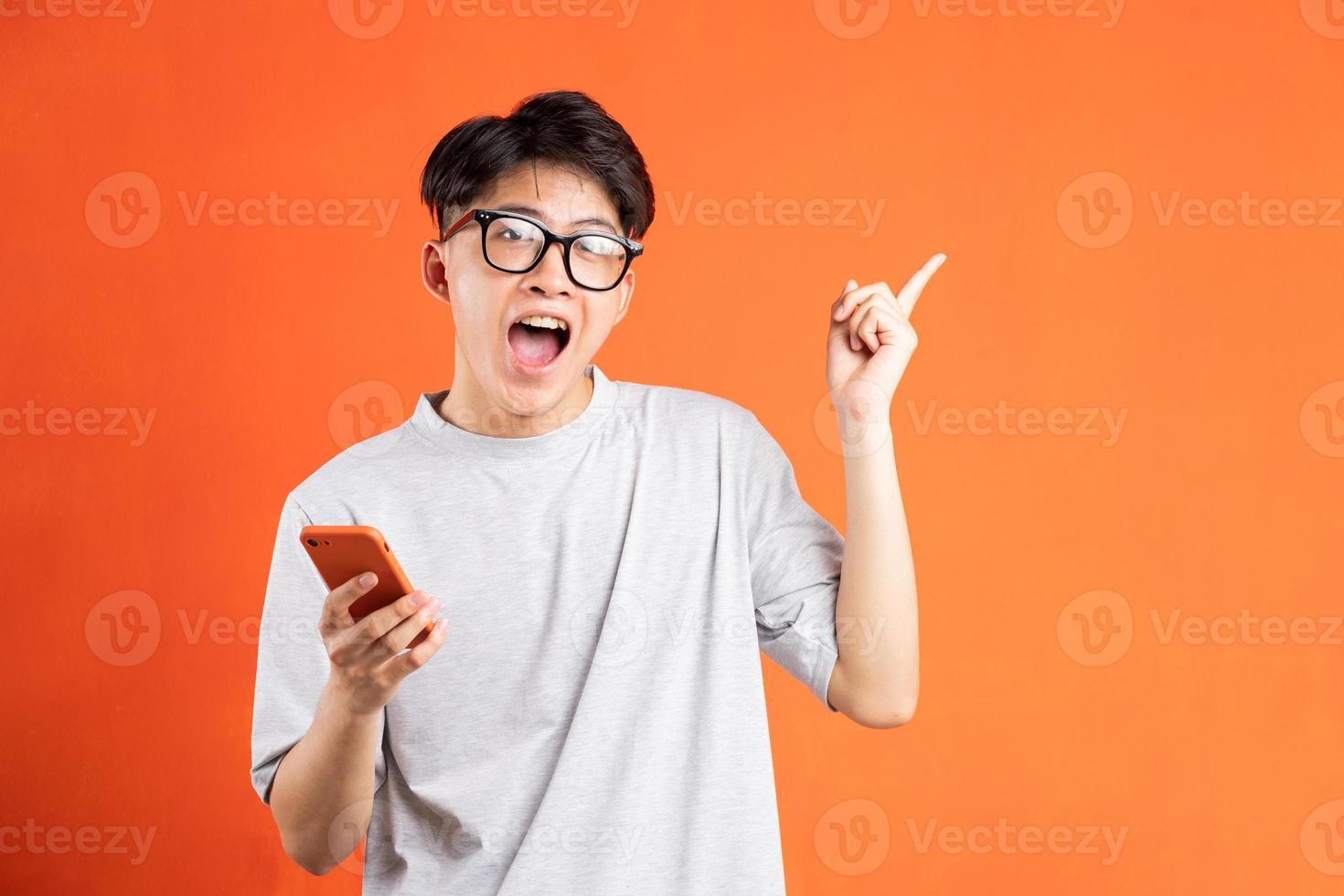 retrato, de, joven, asiático, hombre, en el teléfono, aislado, en, fondo naranja foto