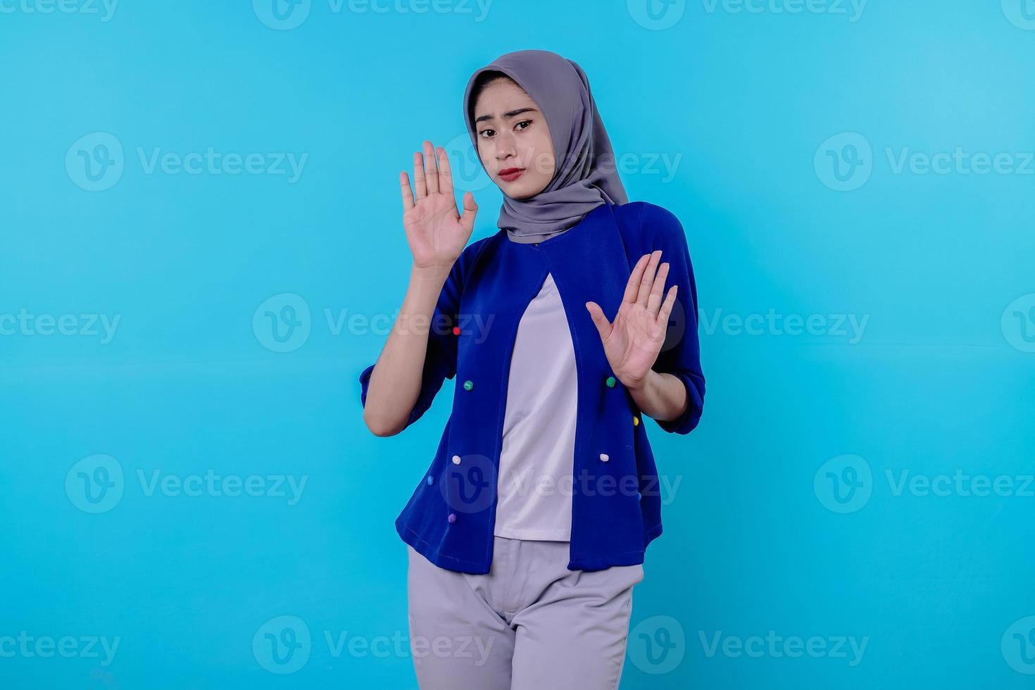 portrait of a woman wearing hijab showing stop gesture on blue wall photo