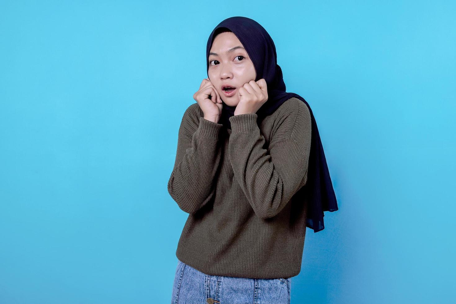 Intense afraid woman wearing hijab feeling scared and shocked and staring with popped eyes on blue wall photo