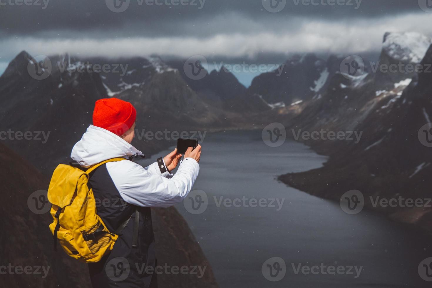 Man traveler taking photo with a smartphone hiking on Reinebringen mountain ridge in Norway lifestyle adventure traveling