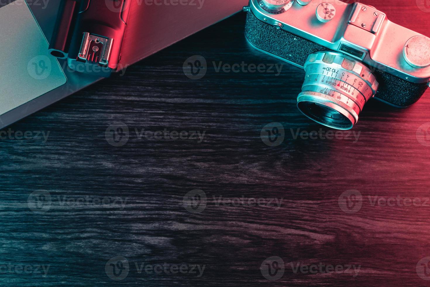 Old film camera and laptop on table. Blue and red light. Copy Space photo