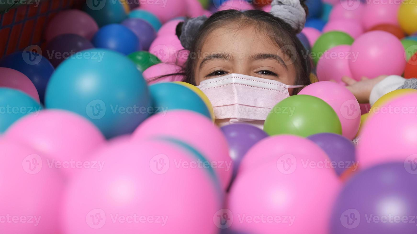 Feliz niña de 5 años con máscara en una piscina de bolas lanzando bolas a la cámara foto