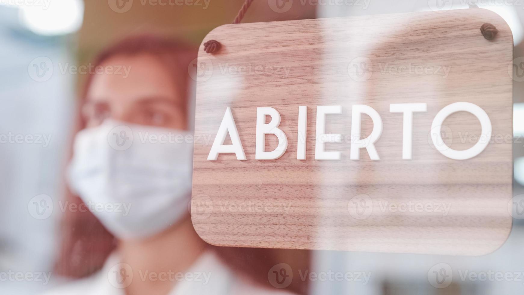 Feliz niña de pequeñas empresas cambiando de signo cerrado a abierto en español en la ventana sonriendo mirando afuera foto