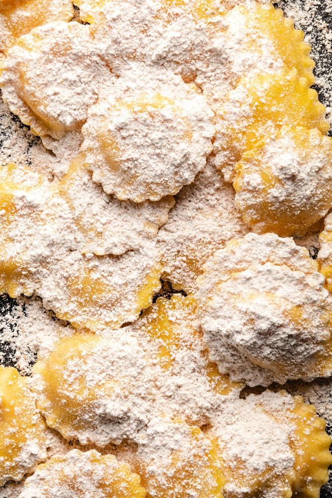 Tasty raw ravioli with flour and basil on wood table photo