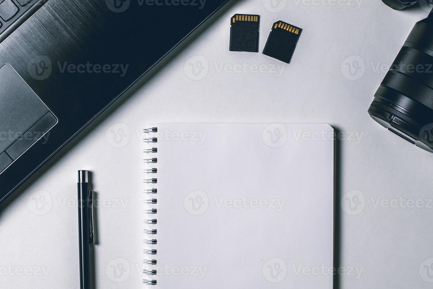 Modern white office desk table with laptop, camera and other supplies. Blank notebook page for input the text in the middle. Top view, flat lay. photo