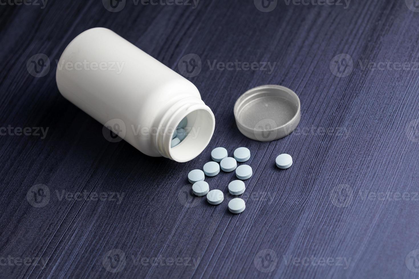Medication bottle and blue pills spilled over blue wood background. Pharmaceutical drugs. photo