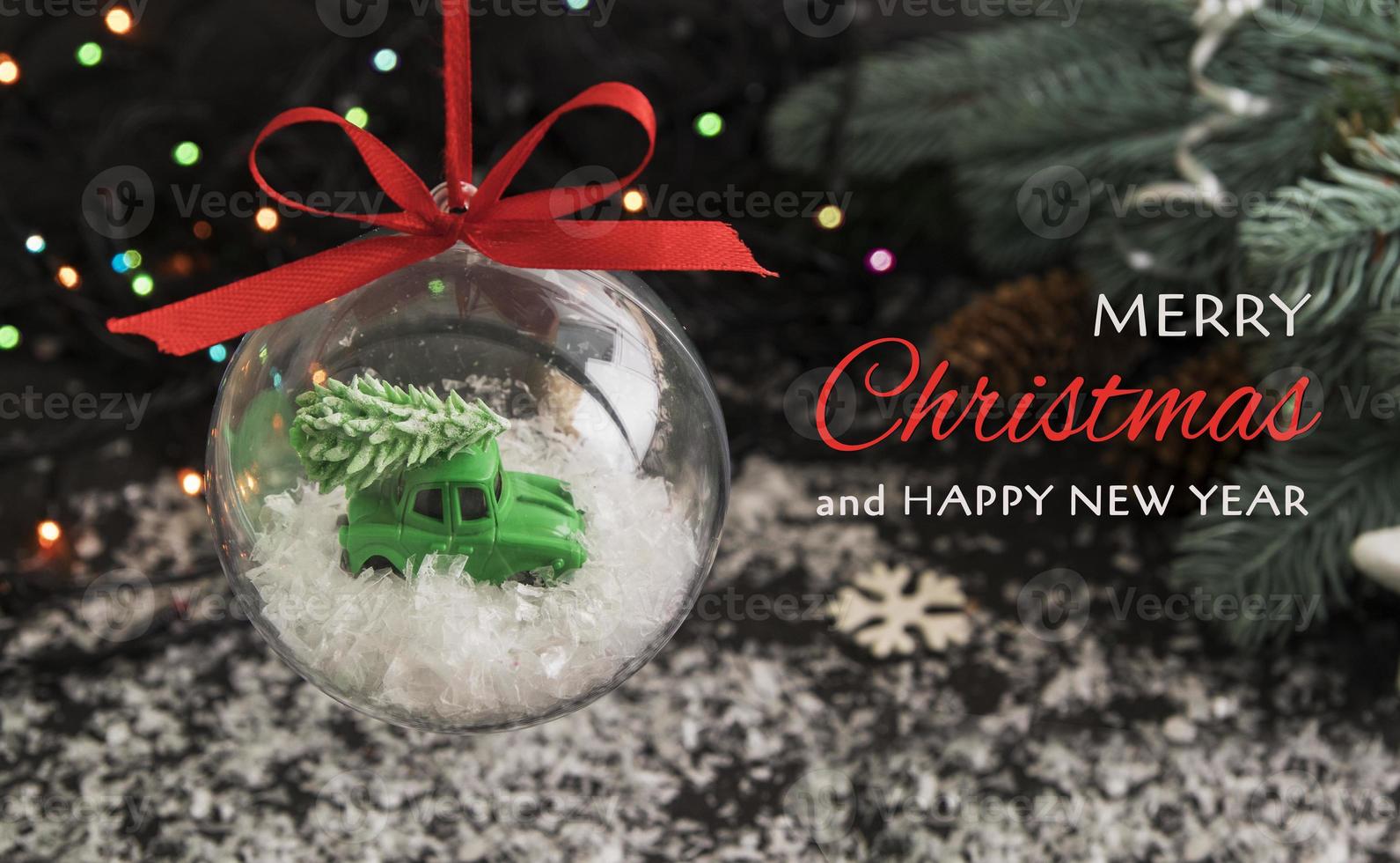 Merry christmas and new year on the background of a transparent ball with a toy car and a tree on the roof in the snow photo