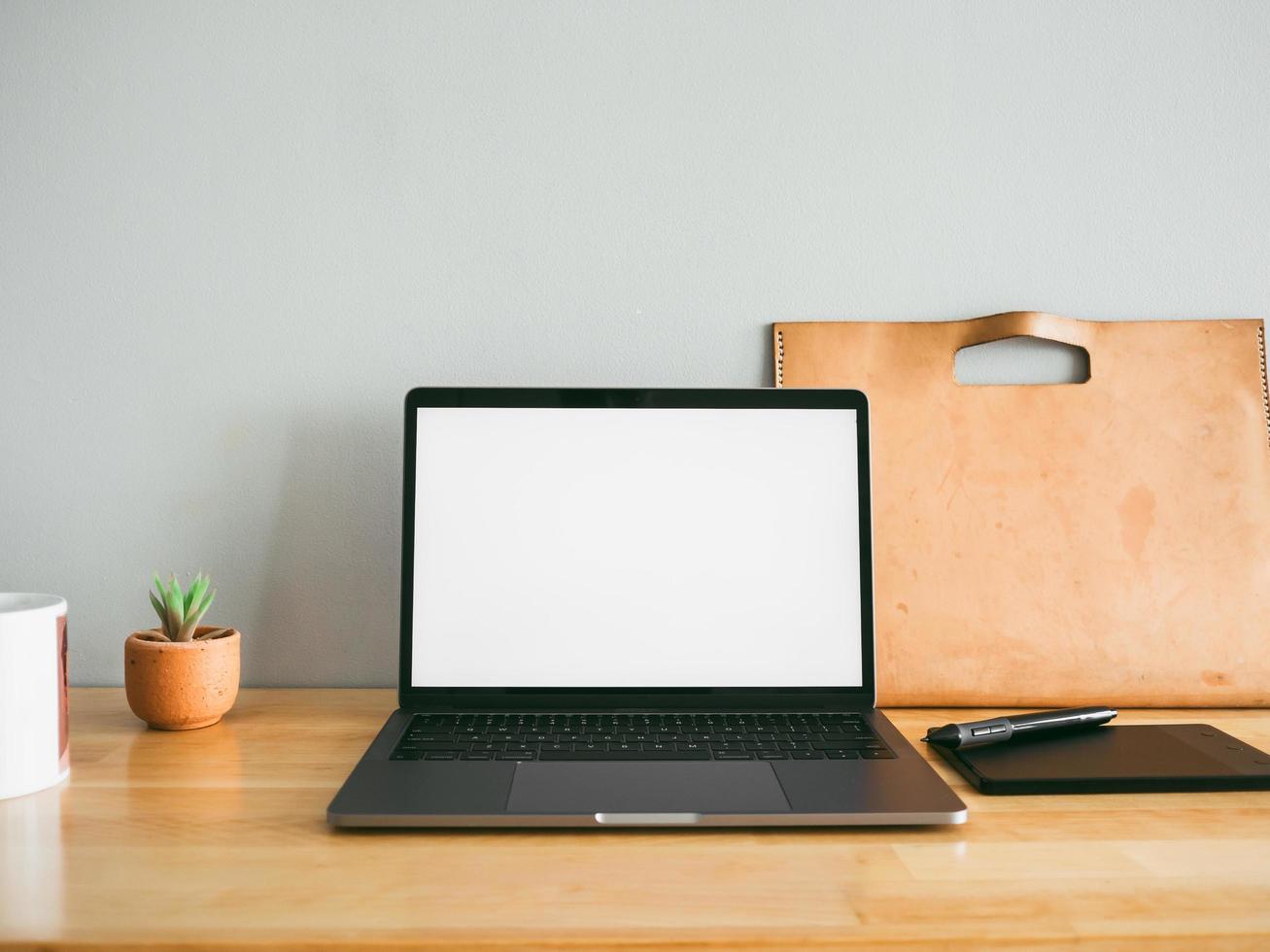 Laptop and some stationary tools on wooden work desk with empty gray wall as background. Concept of workspace and minimal office. photo
