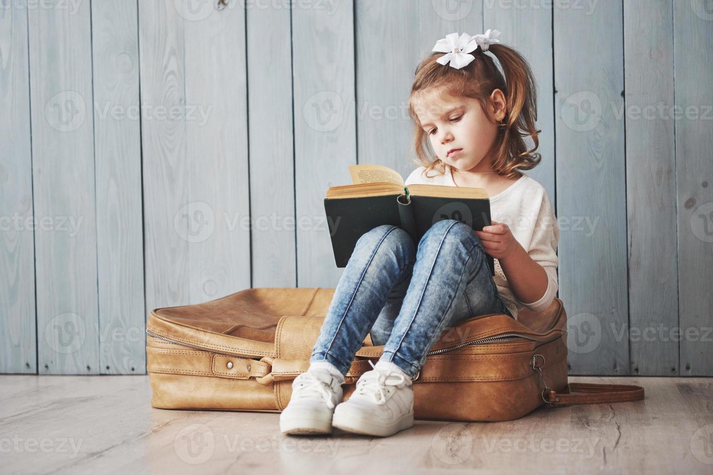 listo para grandes viajes. niña feliz leyendo un libro interesante con un maletín grande. concepto de libertad e imaginación foto