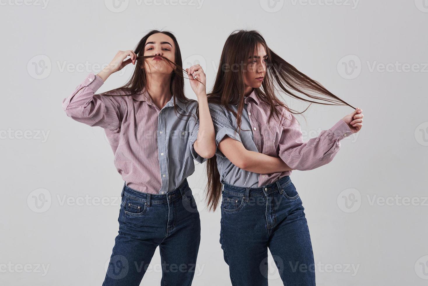 Just fooling around. Two sisters twins standing and posing in the studio with white background photo