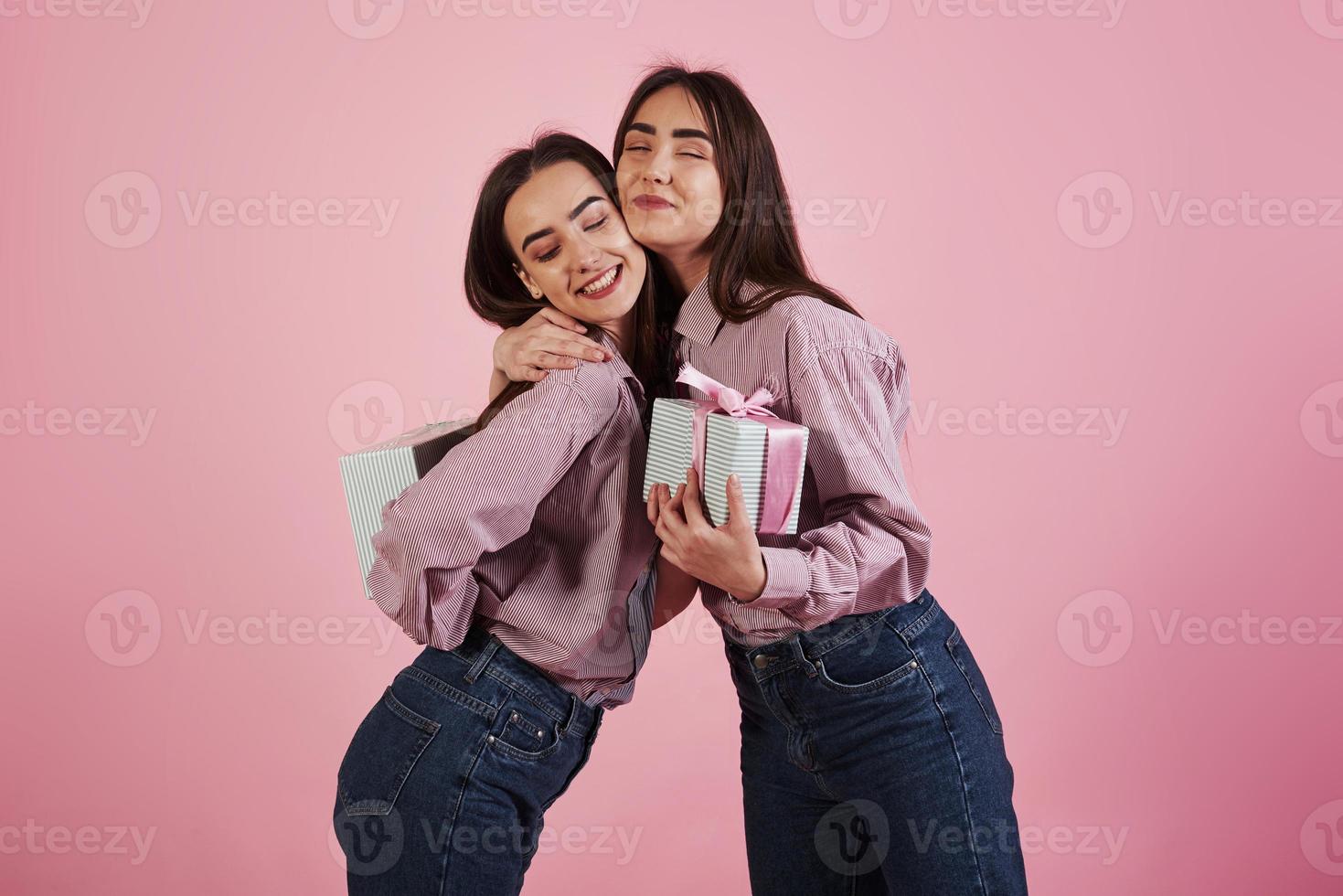 celebrando juntos. mujeres jóvenes divirtiéndose en el estudio con fondo rosa. gemelos adorables foto
