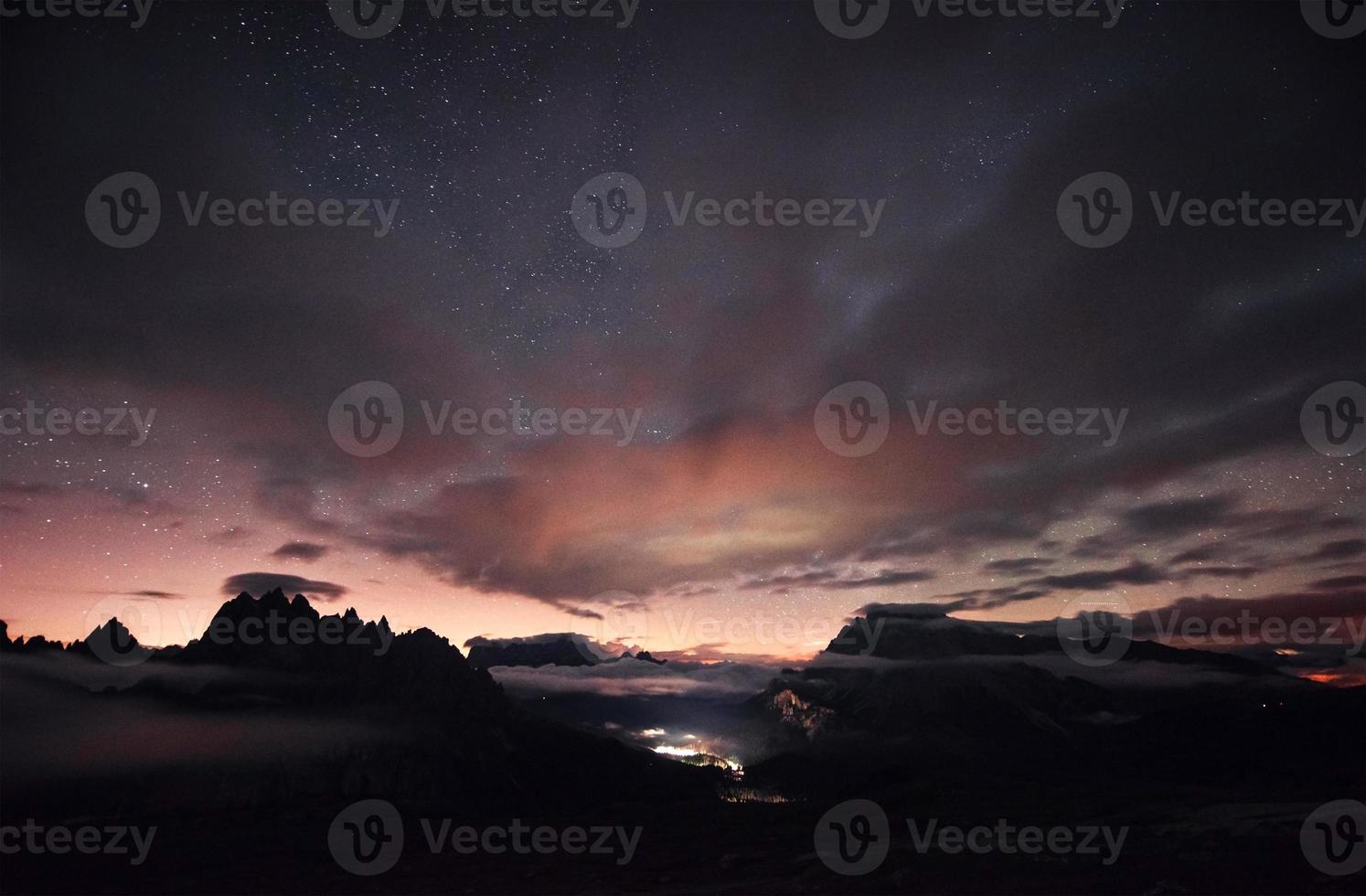 algo brilla en medio del bosque. hermoso espacio lleno de estrellas en el cielo. las montañas están rodeadas de una densa niebla foto