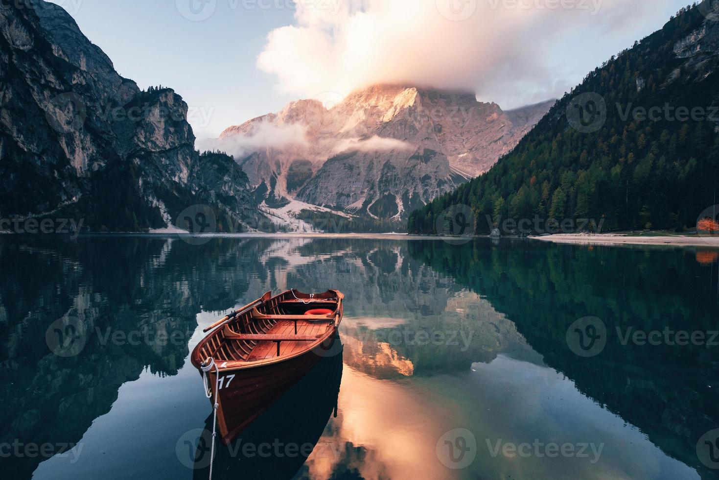 Tarde cálida y soleada. barco de madera en el lago de cristal con majestuosa montaña detrás. reflejo en el agua foto