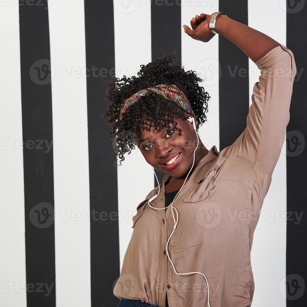 mujer alegre. Sonrió niña afroamericana se encuentra en el estudio con líneas verticales blancas y negras en el fondo foto