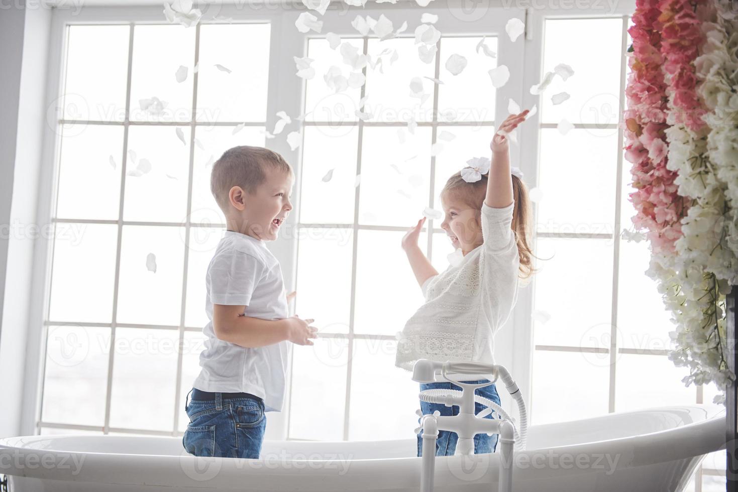 Child playing with rose petals in home bathroom. Little girl and boy fawing fun and joy together. The concept of childhood and the realization of dreams, fantasy, imagination photo