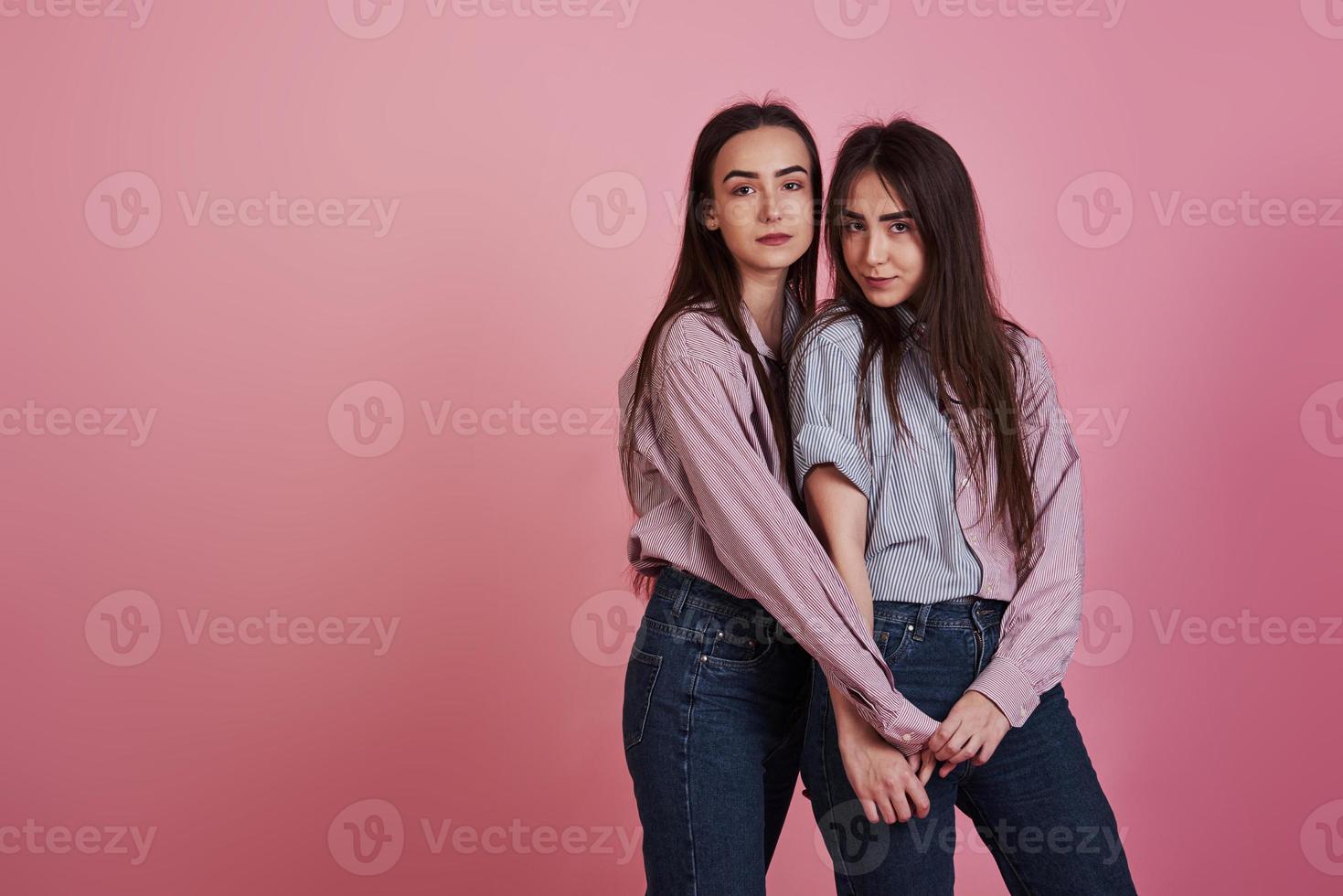 Young women having fun in the studio with pink background. Adorable twins photo