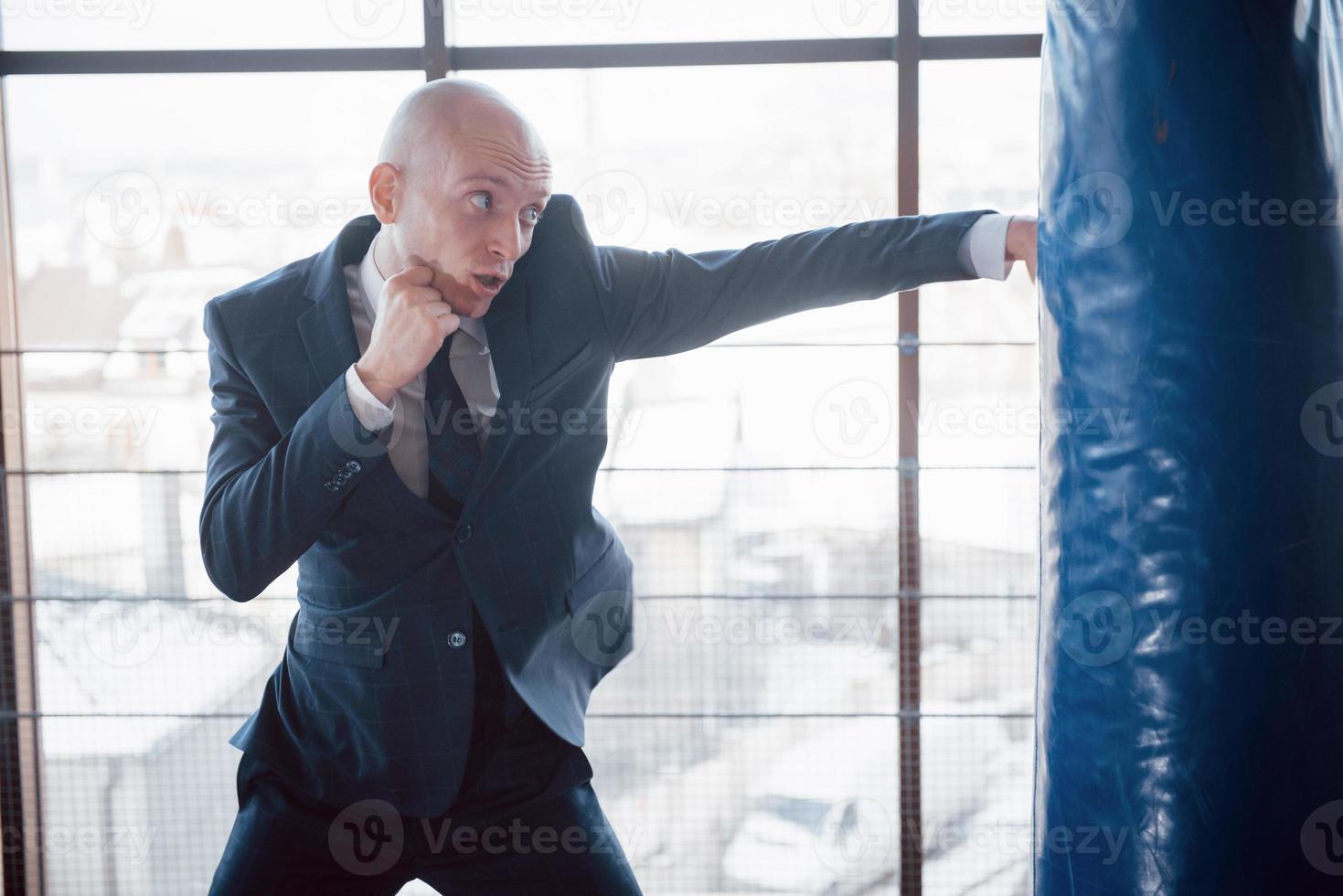 un hombre de negocios calvo enojado golpea una pera de boxeo en el gimnasio. concepto de manejo de la ira foto