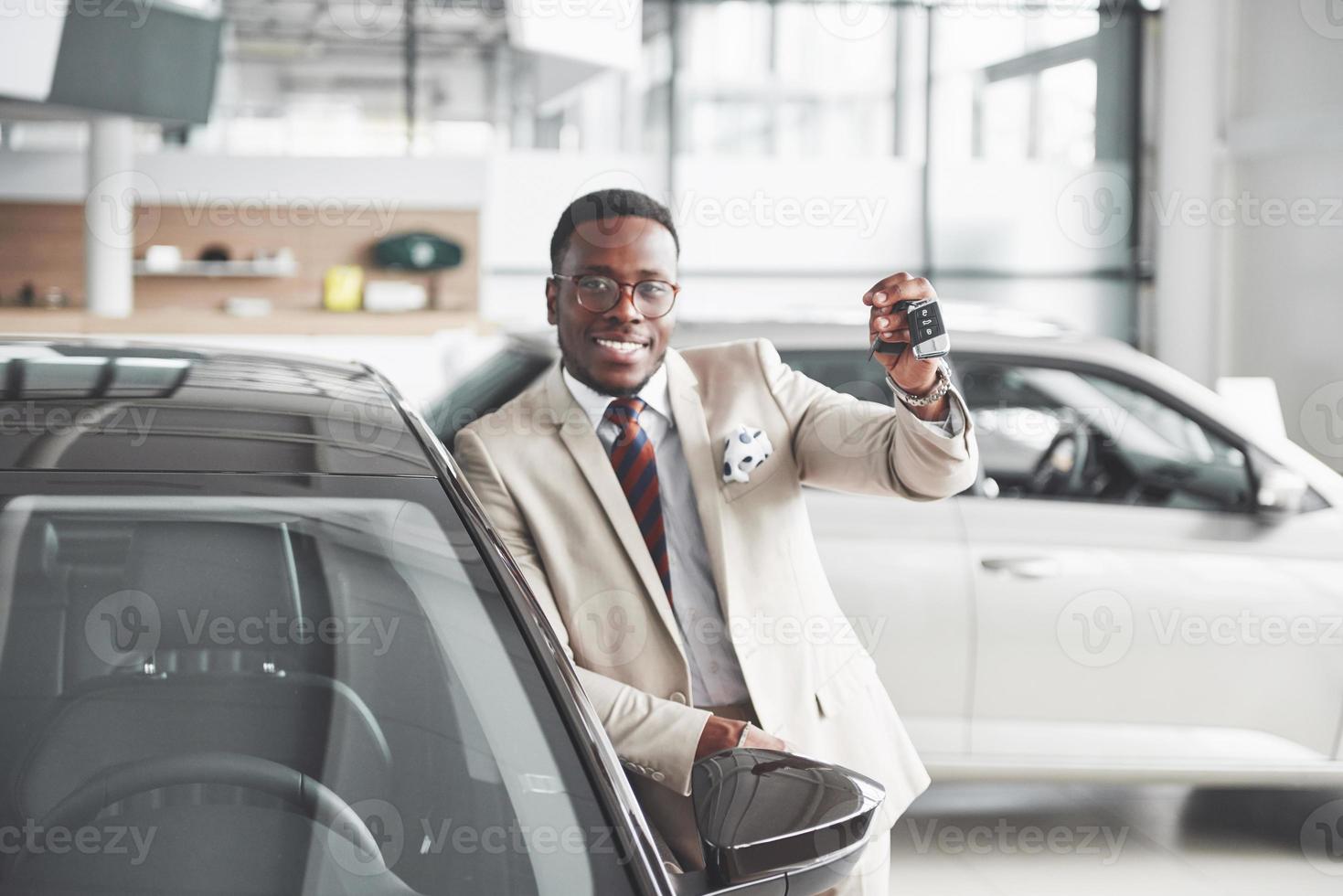 Handsome black man in dealership is hugging his new car and smiling photo