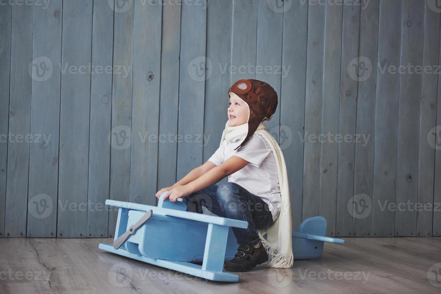 Happy kid in pilot hat playing with wooden airplane against. Childhood. Fantasy, imagination. Holiday photo