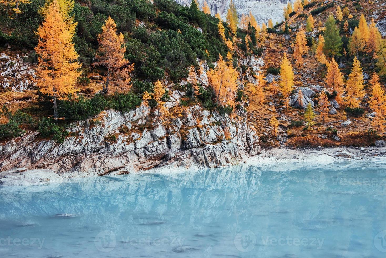 día de otoño en las majestuosas montañas. árboles de color amarillo en las rocas. hermoso lago de cristal azul foto