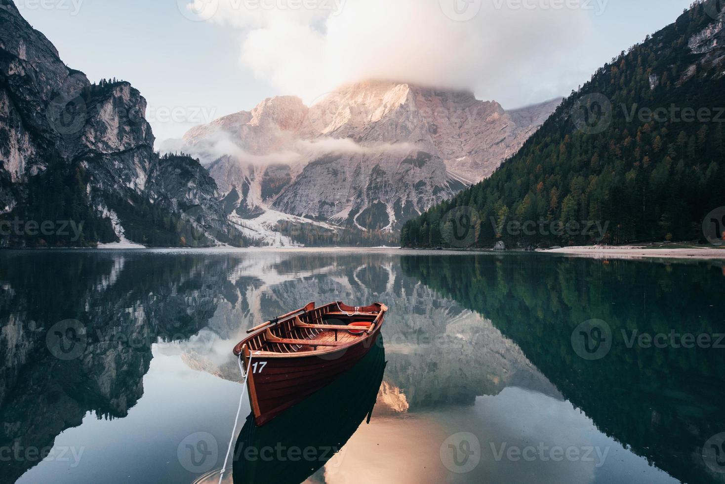It's adventure time. Wooden boat on the crystal lake with majestic mountain behind. Reflection in the water photo