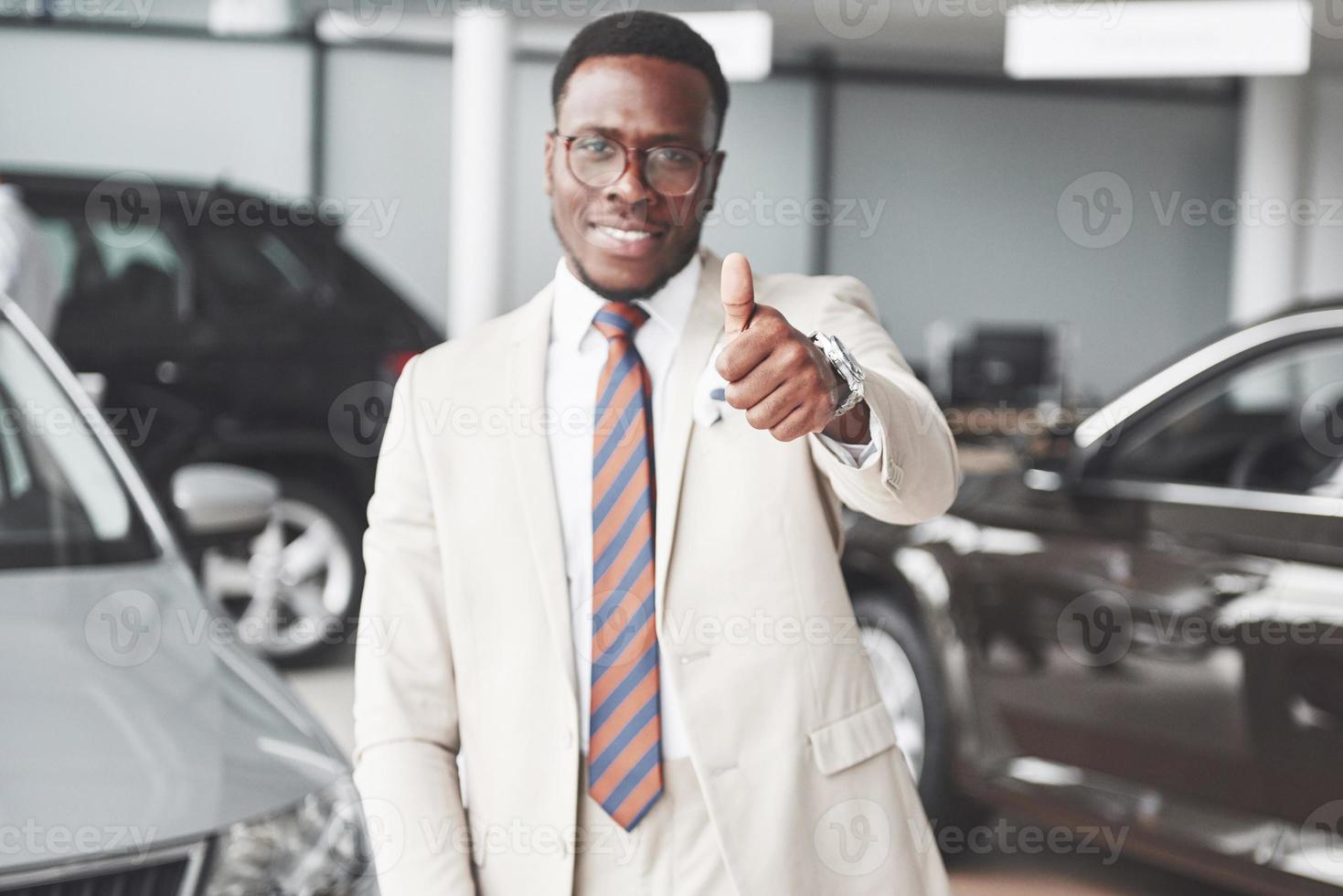 joven empresario negro en el fondo del salón del automóvil. concepto de venta y alquiler de coches. foto