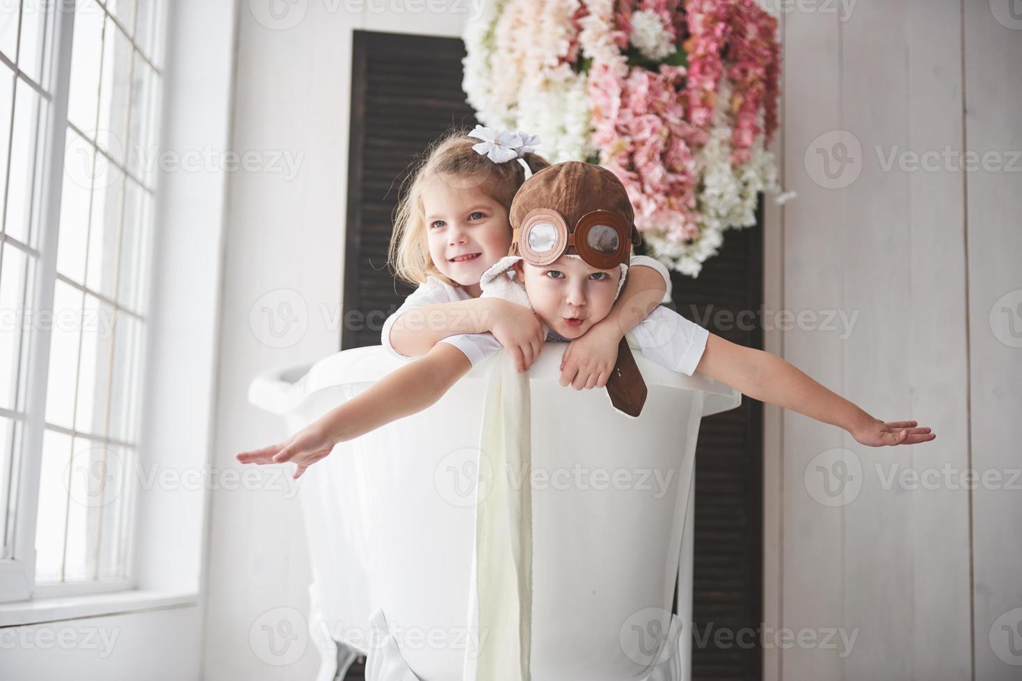 retrato de una niña y un niño con sombrero de piloto jugando en el baño a los pilotos o marineros. el concepto de viaje, infancia y realización de sueños foto