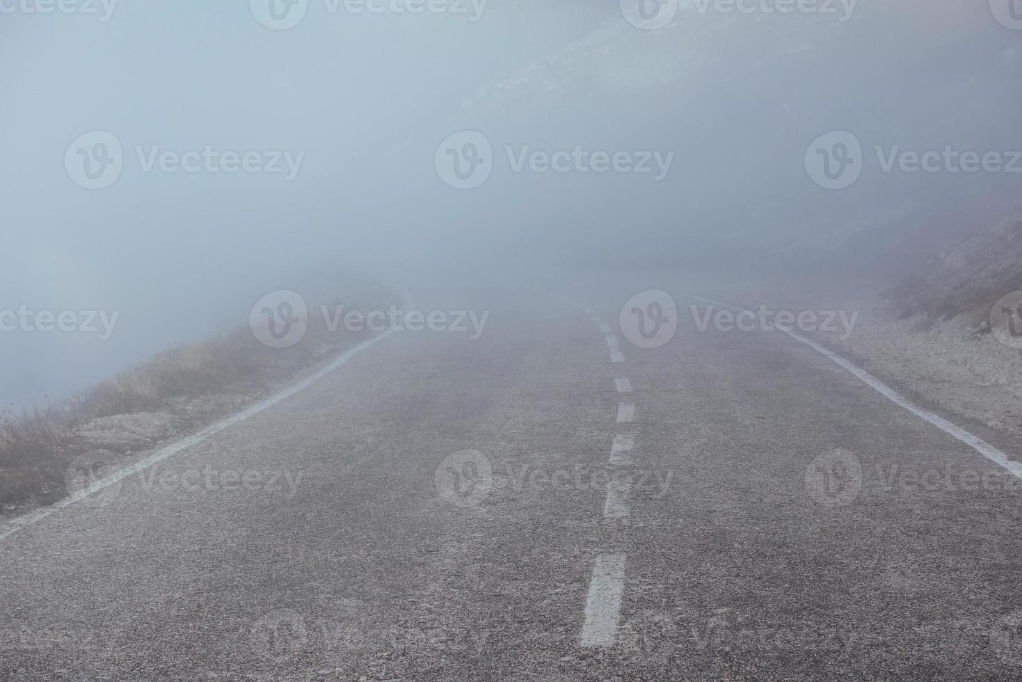 Mysterious looking road in the heavy fog near the mountains photo