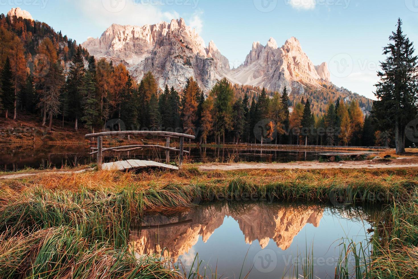 Reflection in the water. Amazing view of majestic mountains with woods in front of them at autumn day. Puddle that goes from the lake with little bridge in the center photo