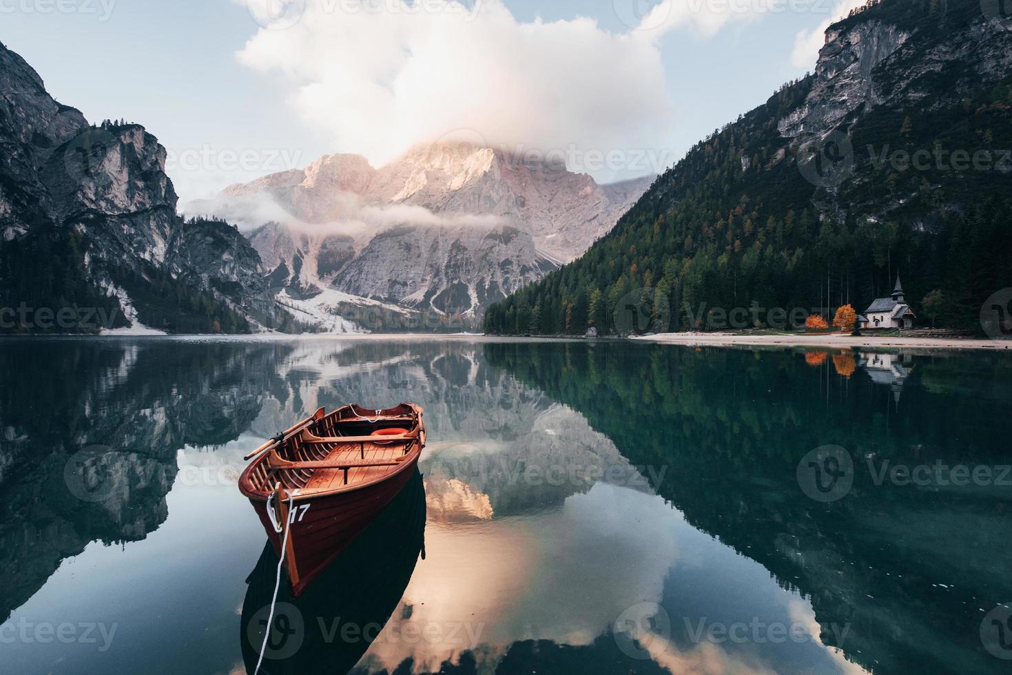 Conception of traveling. Wooden boat on the crystal lake with majestic mountain behind. Reflection in the water. Chapel is on the right coast photo