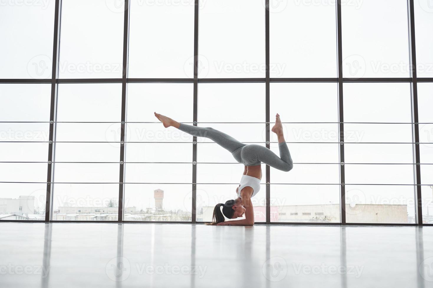 That's how is look results of periodical practice. Side view of girl in sportswear doing stretch exercises in the big spacious gym photo