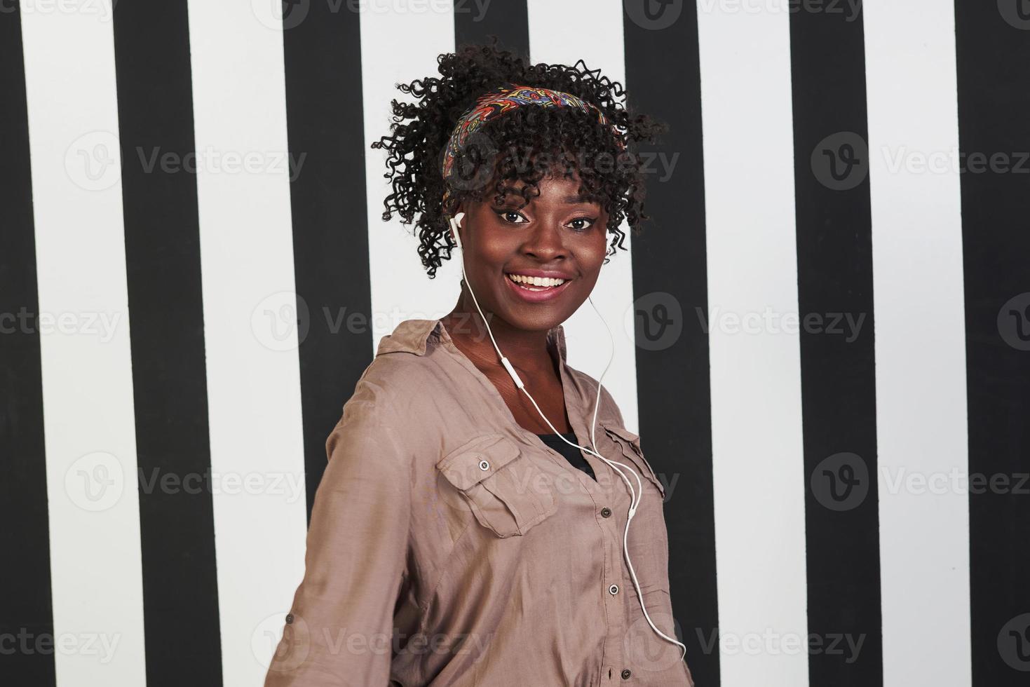 Pure happiness. Smiled afro american girl stands in the studio with vertical white and black lines at background photo