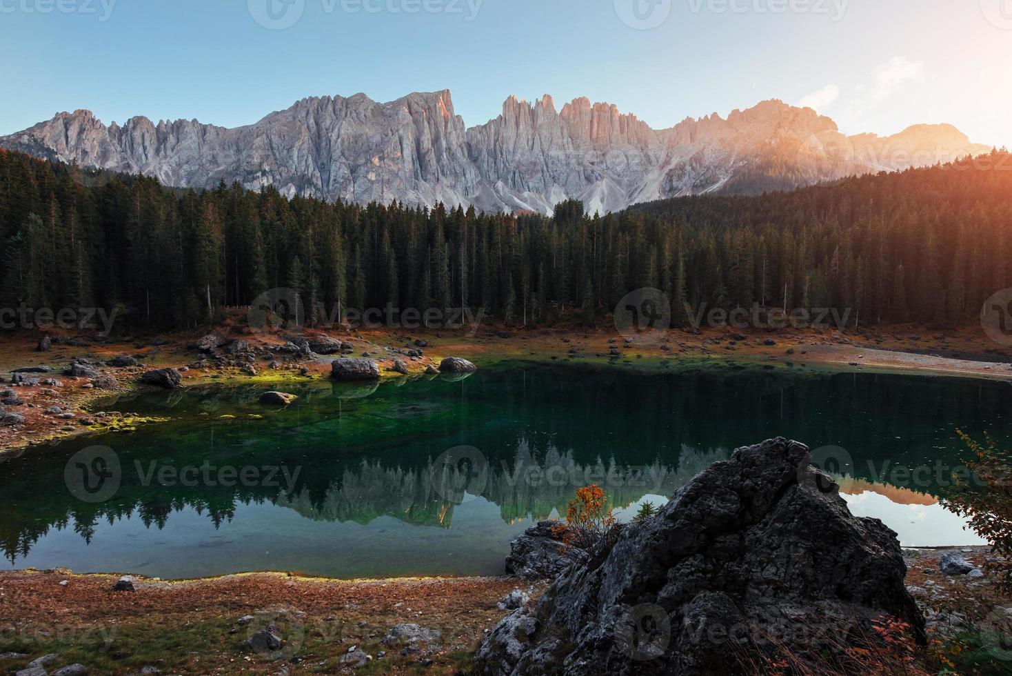 Plants are blooming in the water, you can see it by green color. Autumn landscape with clear lake, fir forest and majestic mountains photo