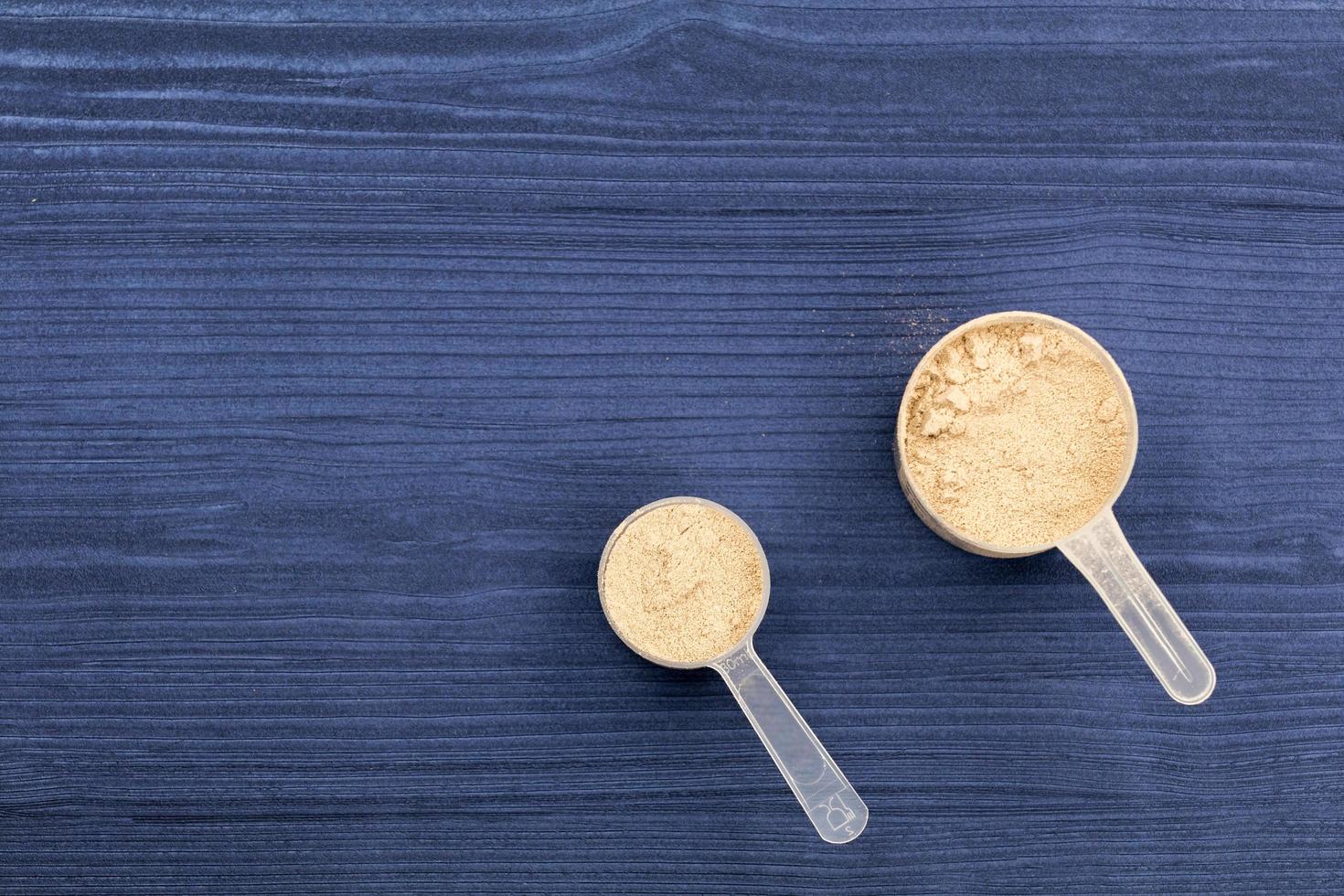 Scoops filled with protein powders on background blue wood photo