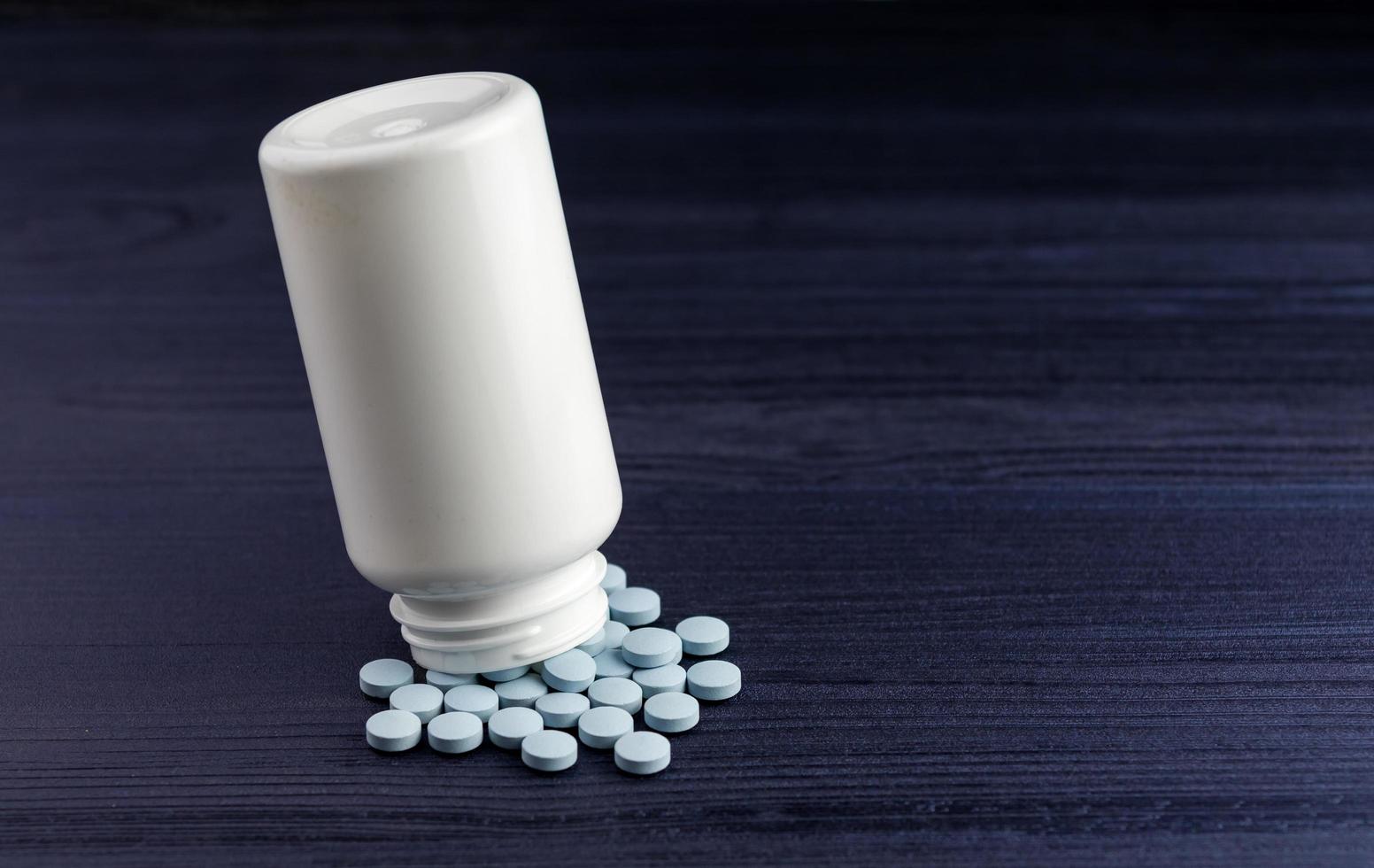 Pills spilling out of pill bottle and blue wood background. View with copy space. Medicine concept photo