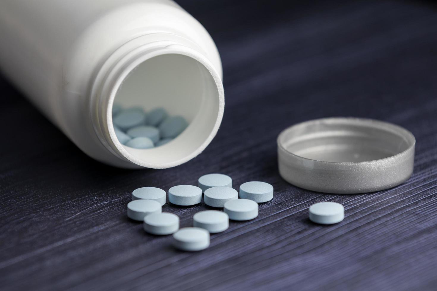 Pills spilling out of pill bottle and blue wood background. View with copy space. Medicine concept photo