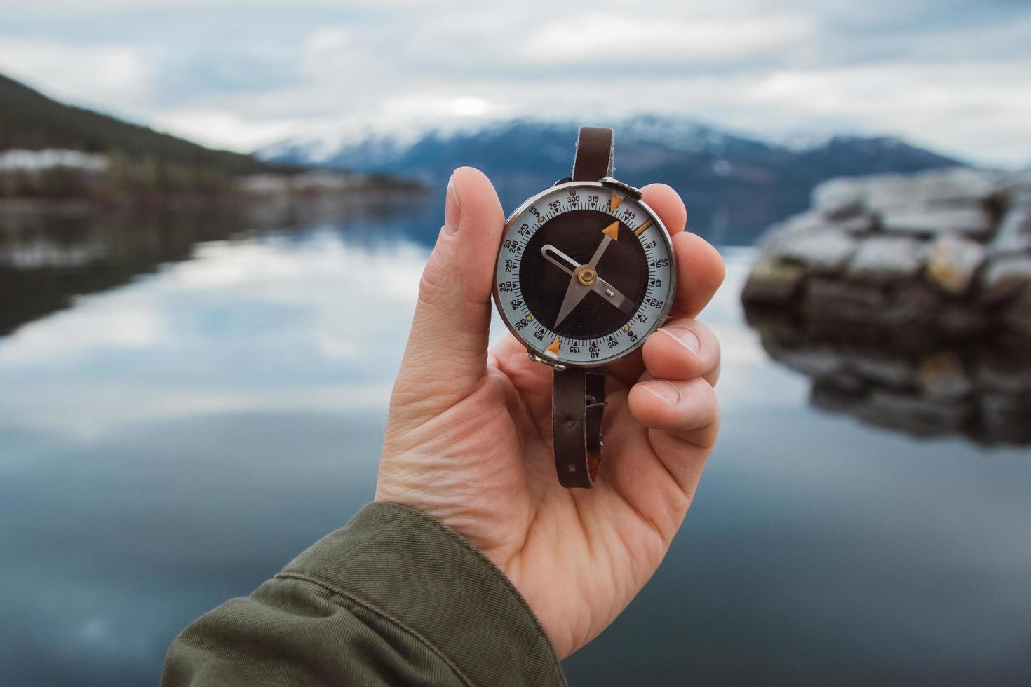 Hermosa mano masculina sostiene una brújula magnética contra el fondo de la montaña y un lago foto