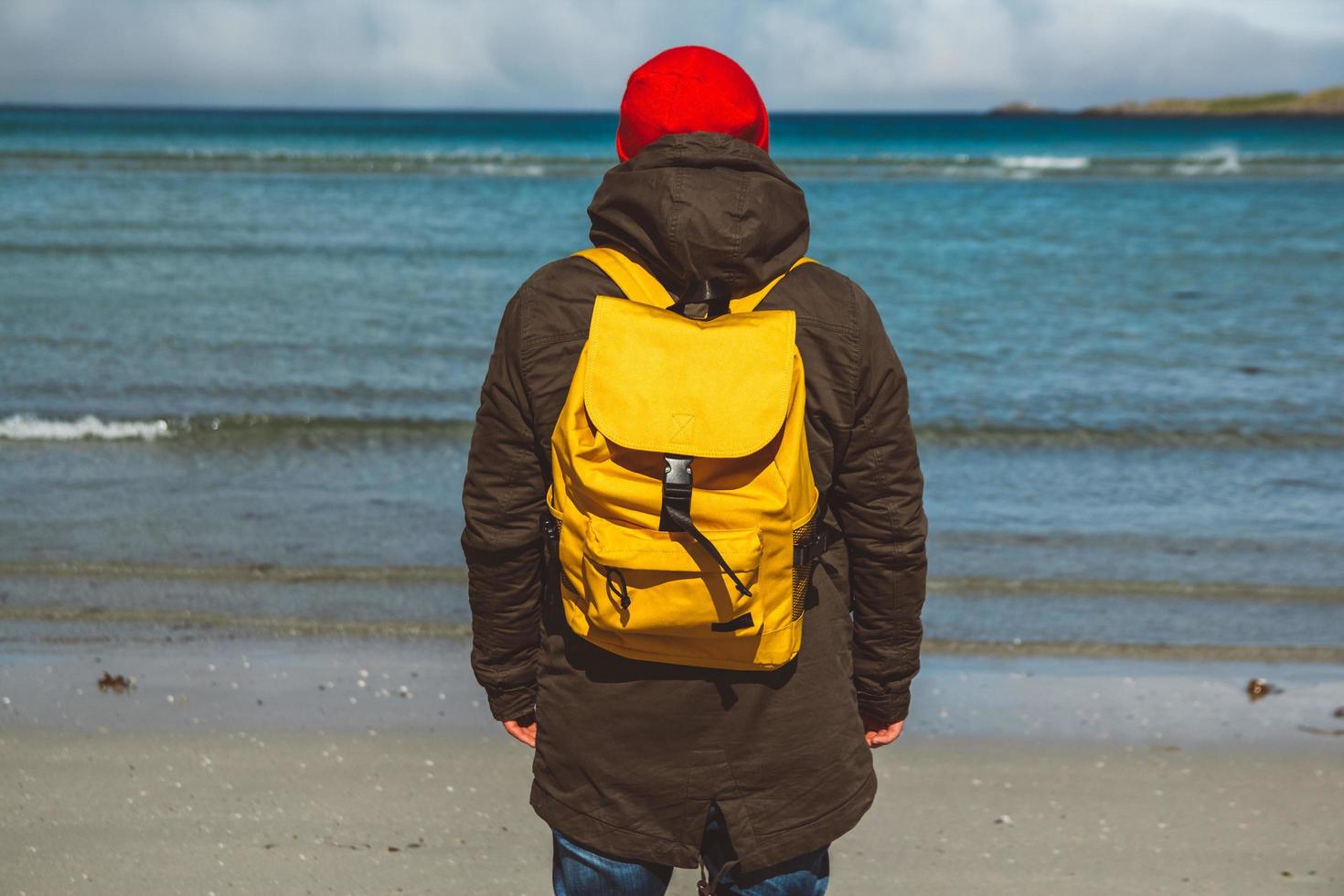 hombre viajero con mochila amarilla con un sombrero de pie en una playa de arena en el fondo del mar. disparar desde la espalda 4064390 Foto de stock en Vecteezy