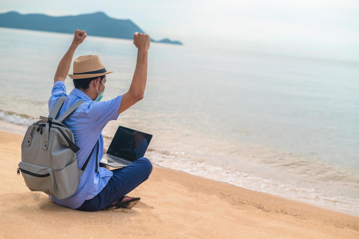 Man wear mask using laptop computer on beach  sea  and Man travel holiday Phuket sandbox Thailand are freedom life financial photo