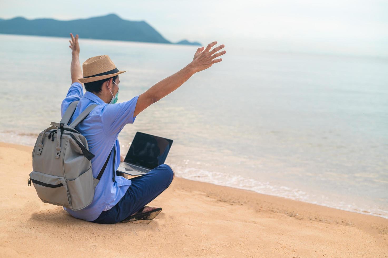 Man wear mask using laptop computer on beach  sea  and Man travel holiday Phuket sandbox Thailand are freedom life financial photo