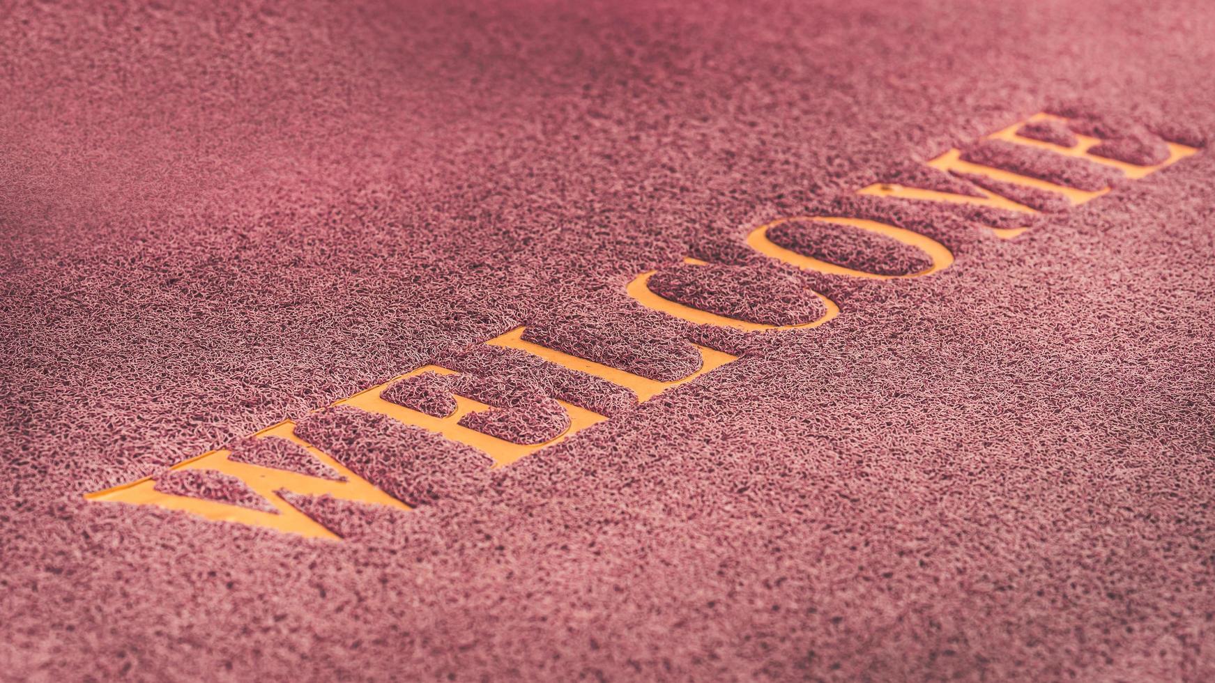 Close-up of welcome message on dark red doormat, background. photo