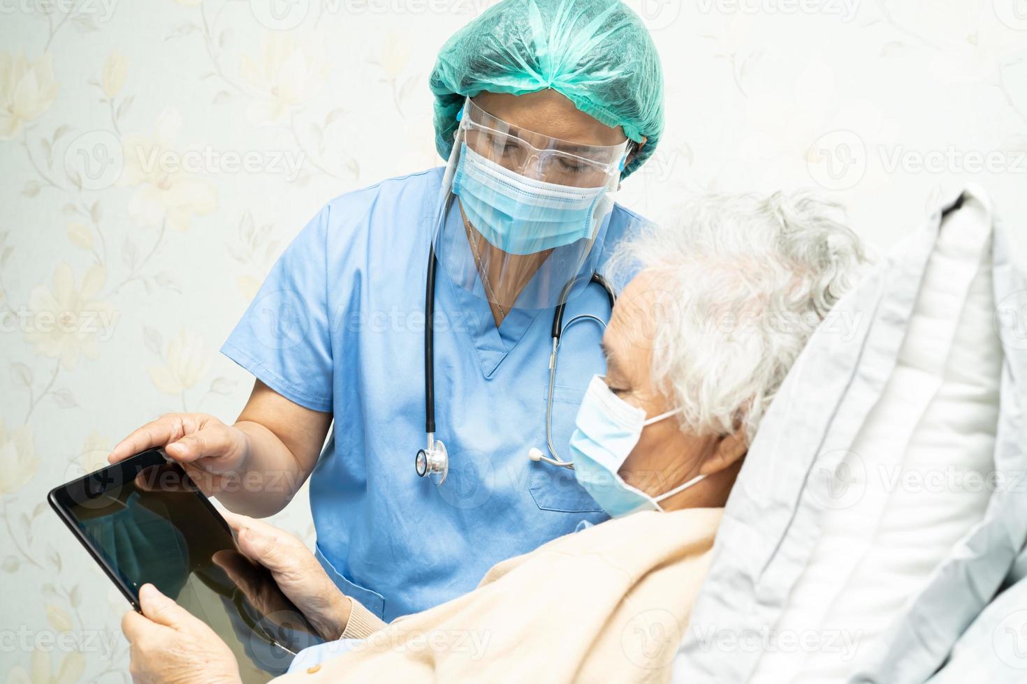 médico con protector facial y traje de ppe nueva tableta digital de sujeción normal para buscar datos sobre infecciones, matar y tratar el nuevo coronavirus con una anciana paciente. foto