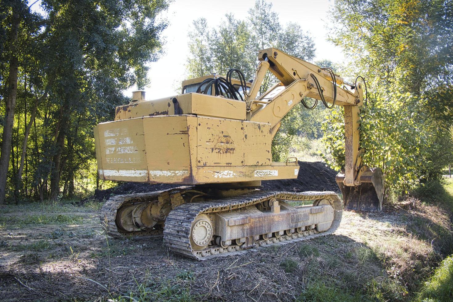 Excavadora con pala mecánica con orugas mientras excavaba en las tierras agrícolas de la langhe piamontesa foto