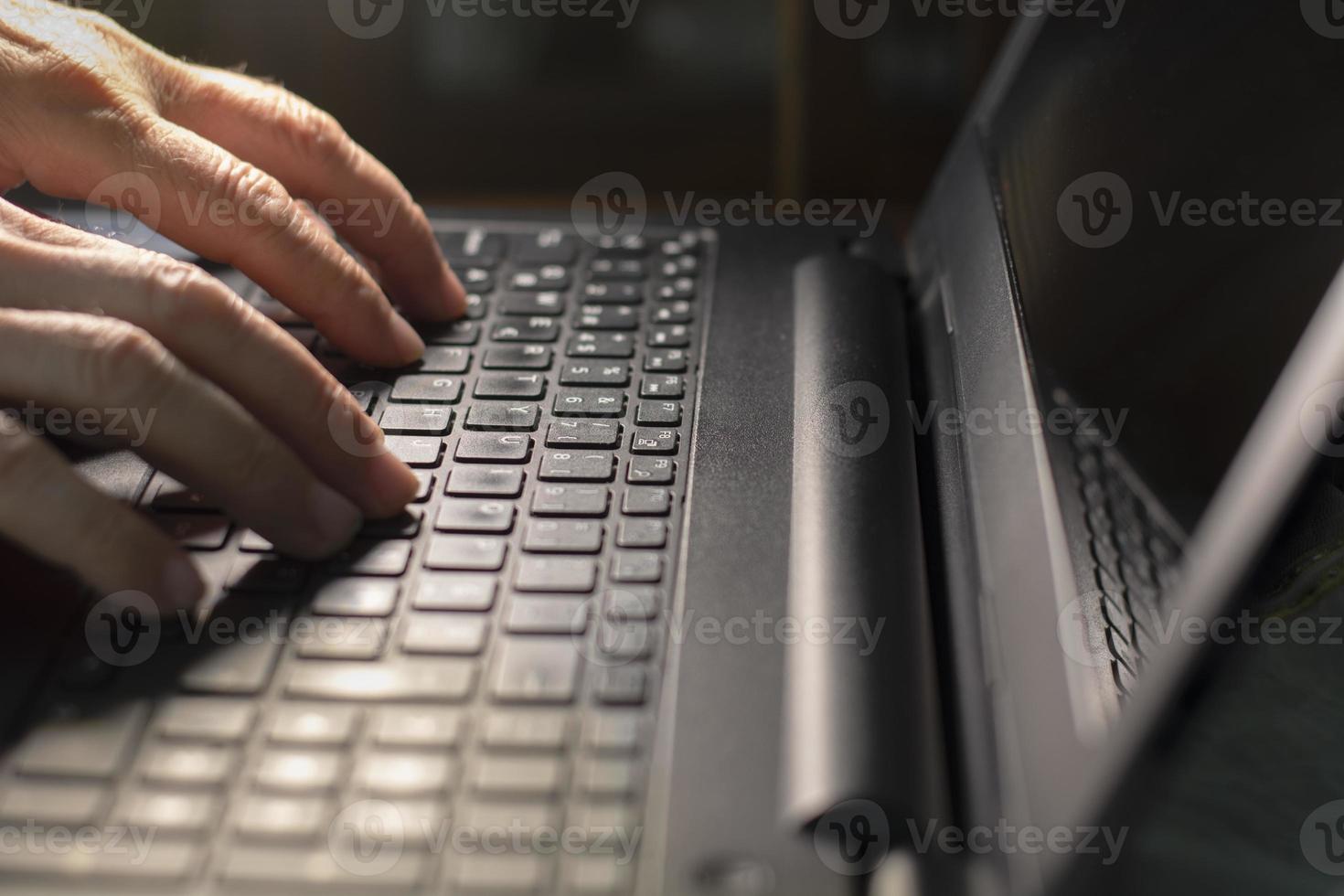 Vista lateral de manos masculinas escribiendo en el teclado del portátil en casa foto