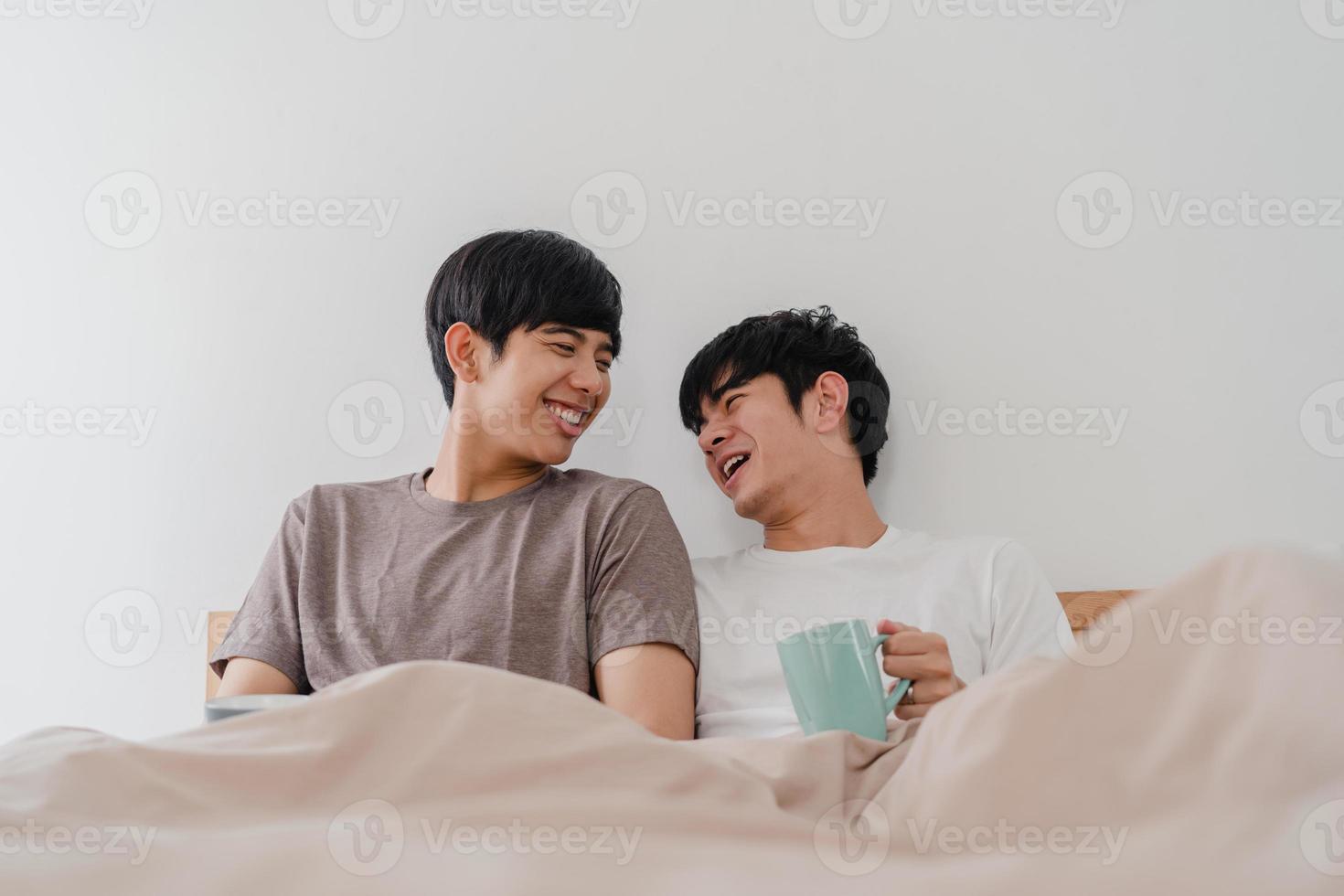 Asian Gay men couple talking having a great time at modern home. Young Asia lover male happy relax rest drink coffee after wake up while lying on bed in bedroom at house in the morning concept. photo